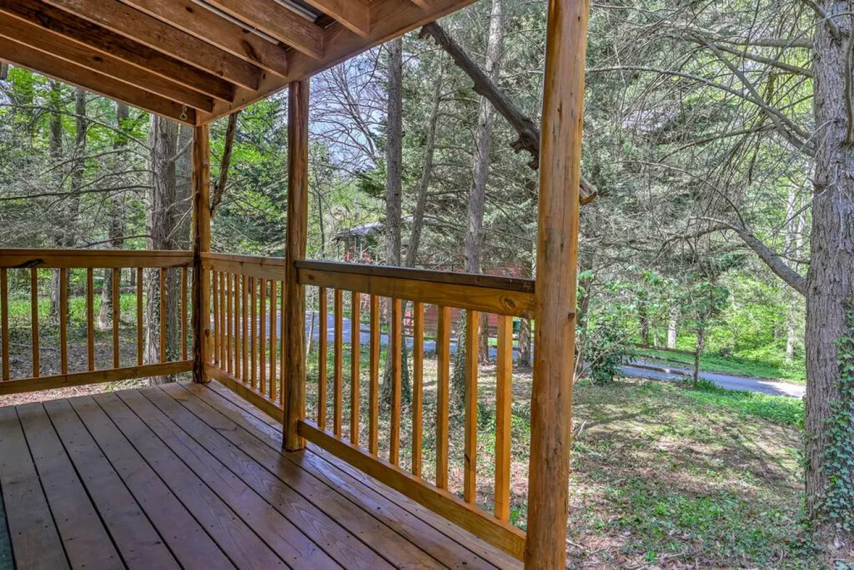 A spacious wooden deck with a sturdy railing overlooks a leafy backdrop of surrounding trees. The deck offers a peaceful spot for relaxing, reading, or letting pets lounge safely outdoors after a day of adventure.