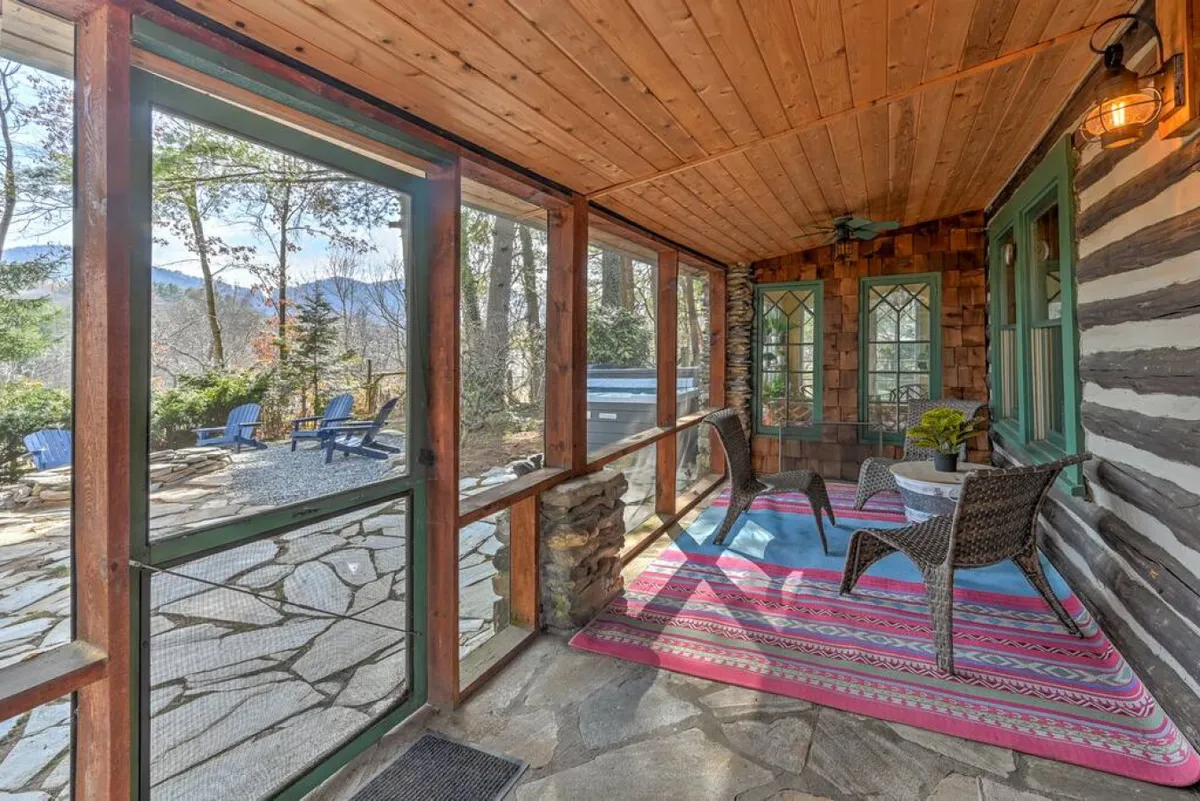 A serene indoor area featuring rocking chairs, colorful rug, and large framed windows looking out toward a hot tub in the background. The space feels both private and welcoming, perfect for sipping morning coffee, reading together, or soaking in the tub while enjoying mountain views.